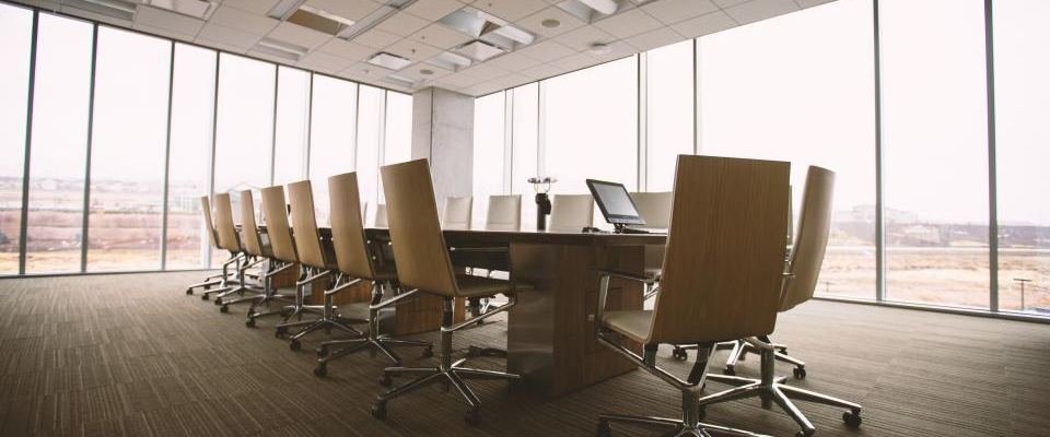 An empty boardroom, a long table, a row of chairs and a screen at the far end.