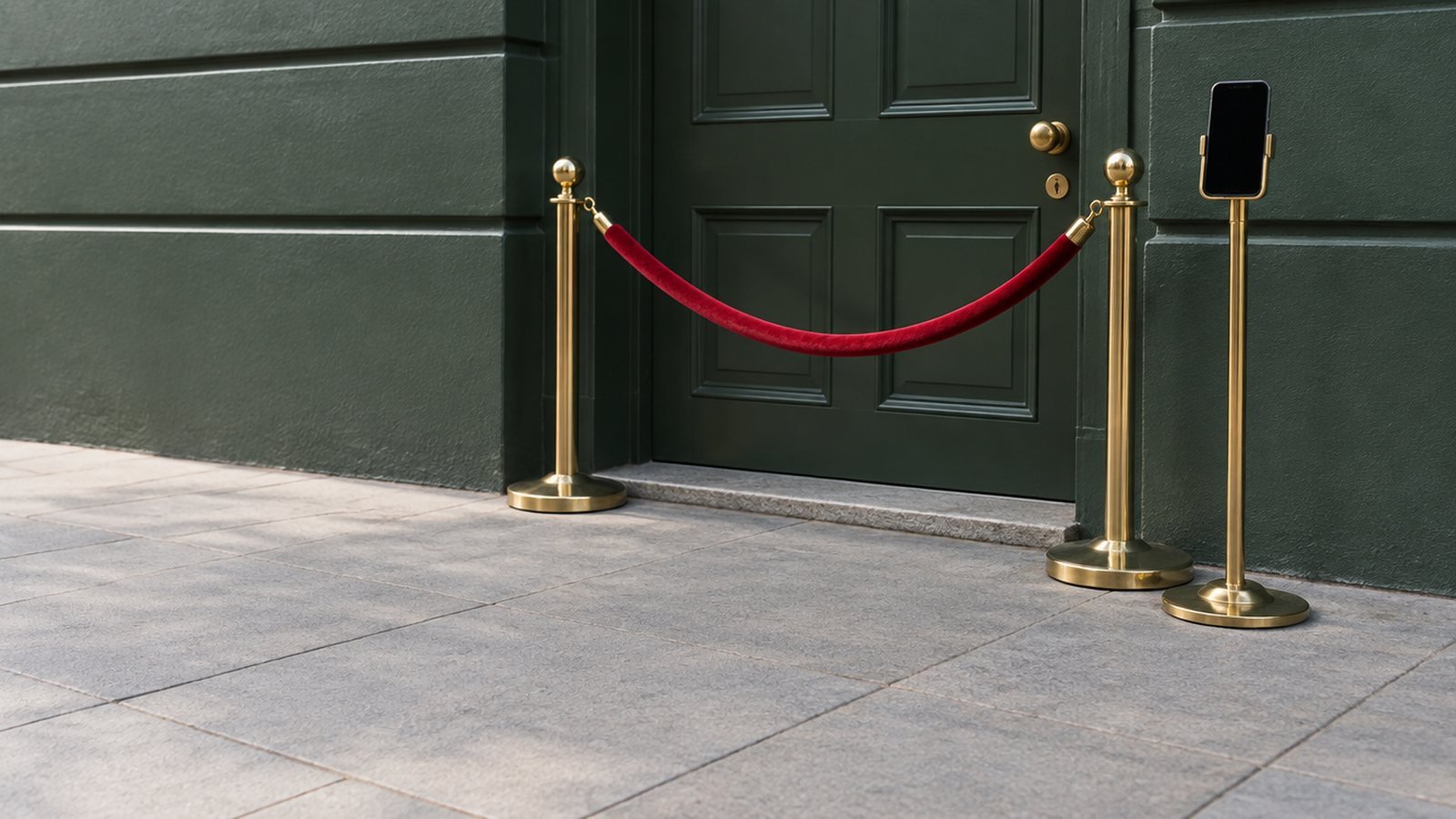 A closed green door roped off with red velvet between brass posts, a smartphone on a brass stand beside it.